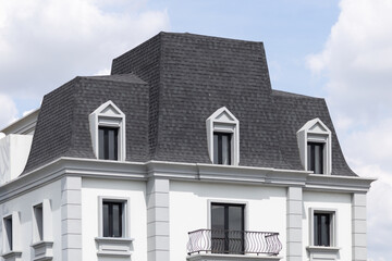 Obraz premium White building with steep gabled roof and three dormers. Roof shingles with garret house on top of the house.