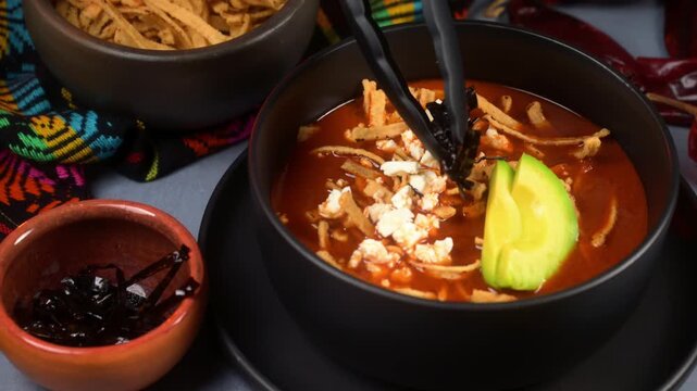 Close up of person adding strips of pasilla chilli to prepare a Mexican tortilla soup, culinary preparation