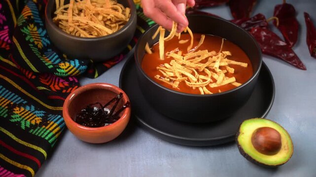 Close up of person adding tortilla strips to prepare a Mexican tortilla soup, culinary preparation