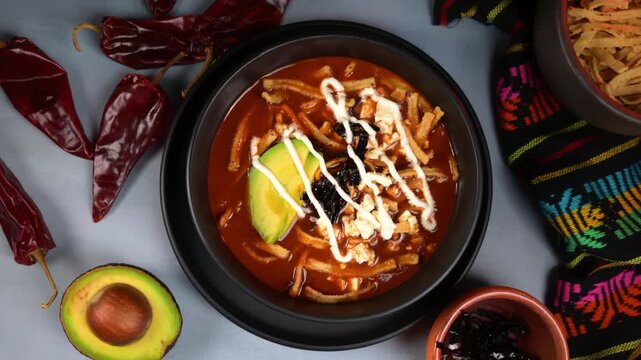Overhead close up of homemade Mexican tortilla soup with fresh ingredients, avocado, tortilla strips and fresh cheese