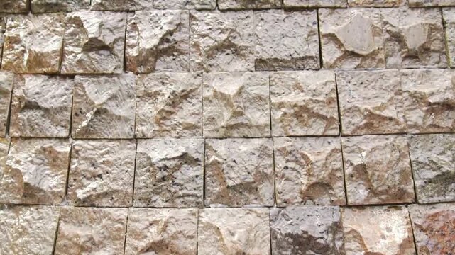 slow upward camera tilt along decorative granite stone block wall texture with water gentle flow down, architectural feature commonly found in hotel, resort, spa, garden and modern landscape design