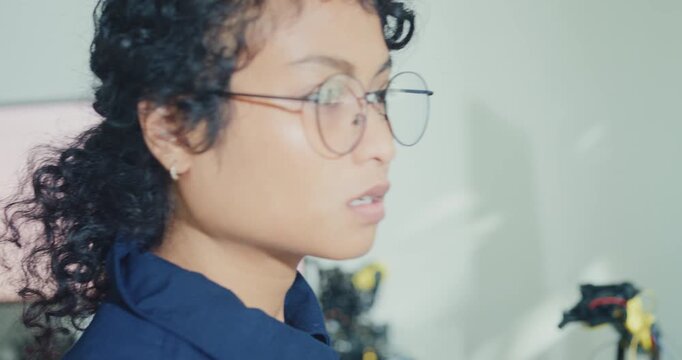 Close-up young Black female robotics engineer coding AI software for robotic arm in laboratory. Embedded system, firmware testing, machine learning, industrial automation, future technology concept.