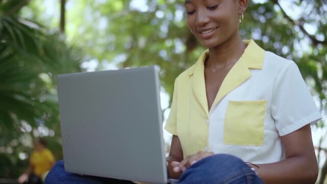 African american female student working outdoors on laptop