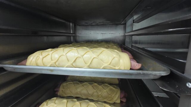 detailed look at rows of raw ham-filled bread with lattice dough patterns being prepared for baking inside a professional industrial oven.