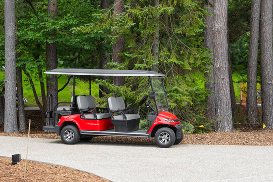 Red golf cart parked on a gravel path by trees