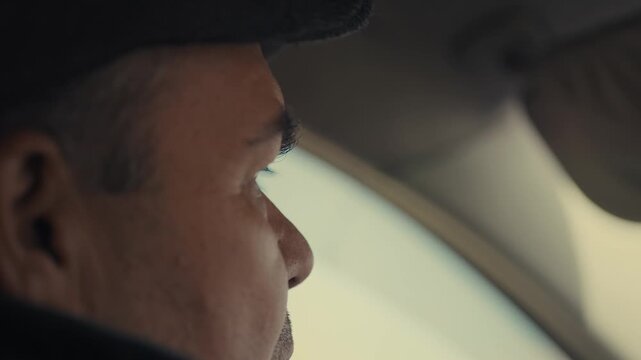 Close-up shows a man's ear. He wears a dark cap. Profile view reveals focused gaze. Eyes look out the car window. Contemplative expression is calm. Ideal for film scenes or introspection