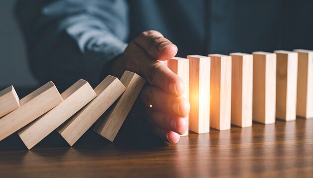 Hand stopping falling wooden domino blocks, symbolizing risk management, crisis prevention, business continuity, resilience, and strategic decision making.