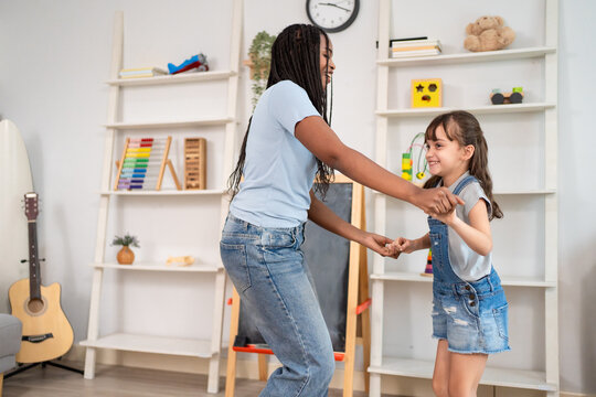 Caucasian young girl and African American nanny dancing in nursery home. 
