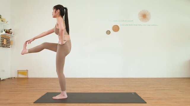 Asian Woman Yoga Instructor Performing Standing Leg Stretch in Fitness Studio
