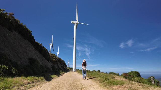 Model released woman standing on a mountain trail below coastal wind turbines