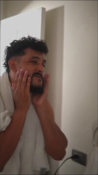Bearded male applying aftershave in bathroom mirror