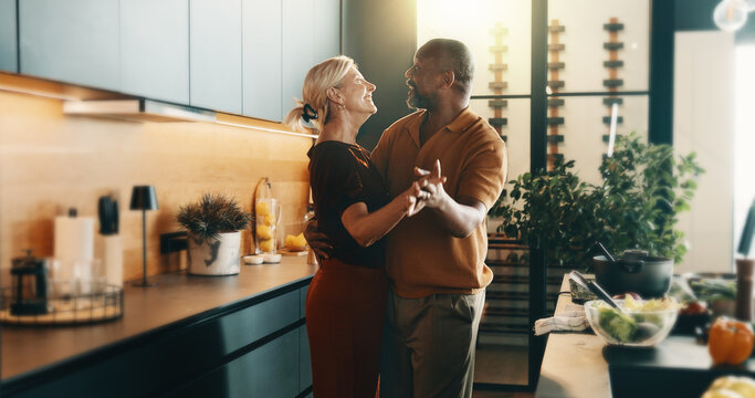 Happy, dancing and mature couple in kitchen for cooking, bonding and love with music, song and meal prep. Interracial, marriage and senior man and woman with radio for dinner, lunch and food in home