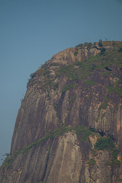 View of Pedra da Gavea with its steep granite cliffs and sparse vegetation under a clear blue sky in Rio de Janeiro, Rio de Janeiro, Brazil.