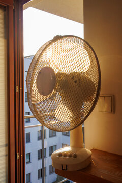 An electric fan standing inside a room at sunrise on a hot summer morning, circulating cool air to improve ventilation during an extreme heatwave.
