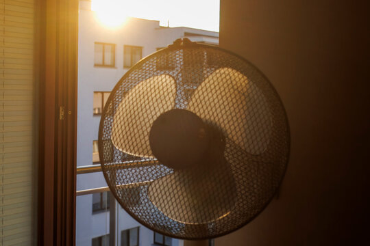 An electric fan standing inside a room at sunrise on a hot summer morning, circulating cool air to improve ventilation during an extreme heatwave.