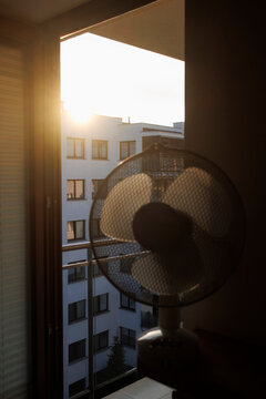 An electric fan standing inside a room at sunrise on a hot summer morning, circulating cool air to improve ventilation during an extreme heatwave.