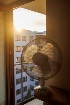 An electric fan standing inside a room at sunrise on a hot summer morning, circulating cool air to improve ventilation during an extreme heatwave.