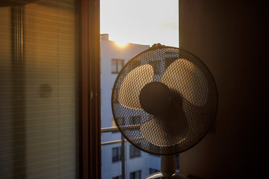 An electric fan standing inside a room at sunrise on a hot summer morning, circulating cool air to improve ventilation during an extreme heatwave.