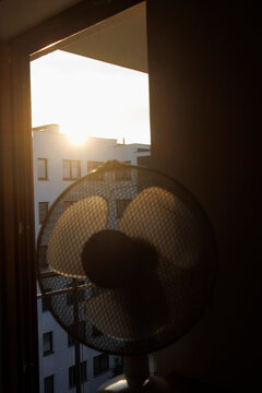 An electric fan standing inside a room at sunrise on a hot summer morning, circulating cool air to improve ventilation during an extreme heatwave.