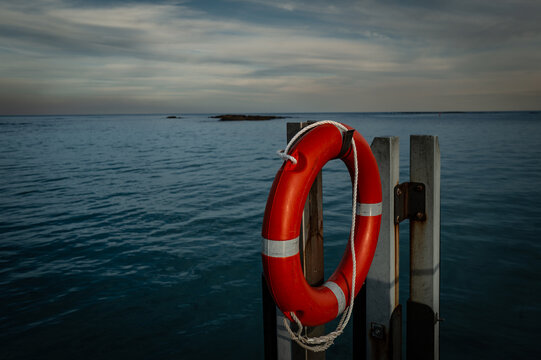 View of a red lifebuoy mounted on a wooden post overlooking the calm ocean waters at sunset in Peaceful Bay, Western Australia, Australia.
