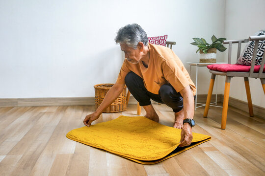 Senior man Crouching Down to Arrange Yellow mat on laminate Floor at Home