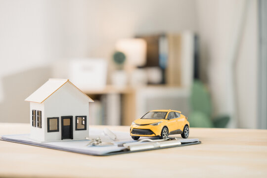 Car model on office desk for finance property planning, monthly payment budget debt cost loan on clipboard with house model helps buyers with real estate investment and mortgage planning