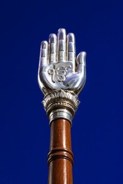 Polished silver hand sculpture featuring the sacred ik onkar symbol attached to a wooden pole