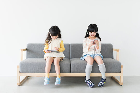 ソファでタブレットとスマートフォンを使う姉妹