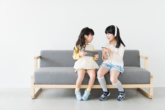 ソファでタブレットとスマートフォンを使う姉妹