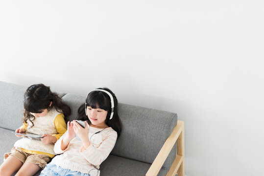 ソファでタブレットとスマートフォンを使う姉妹