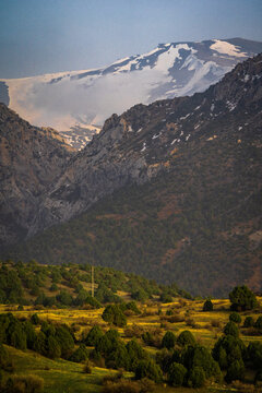 View of the rugged Zaamin mountains featuring snow-capped peaks, dense juniper forests, and rolling hills in Zaamin, Jizzakh Region, Uzbekistan.