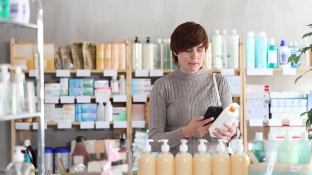 Woman in autumn clothes scans code on package of cream to check the expiration date. High quality 4k footage