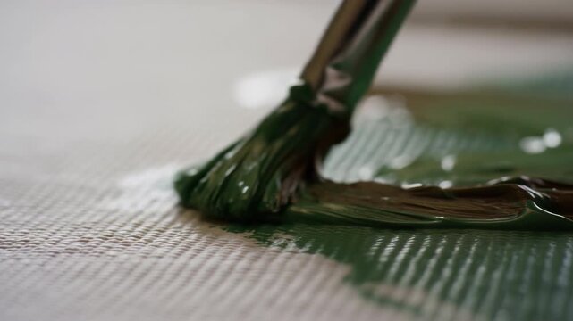 paintbrush dipping and moving through paint on canvas surface close-up top-down perspective creative and artistic expression painting process green white commercial natural light clean.