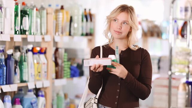 Positive beautiful young woman choosing toothpaste and oral care products in large store