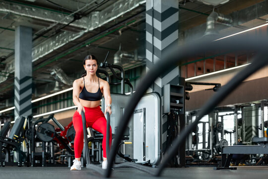 Athletic woman in red leggings doing intense battle ropes workout in gym