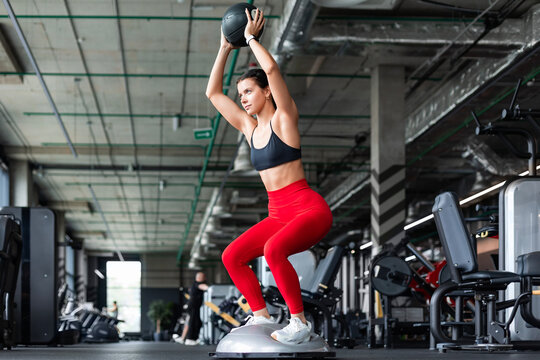 Sporty woman making squats on balance trainer.