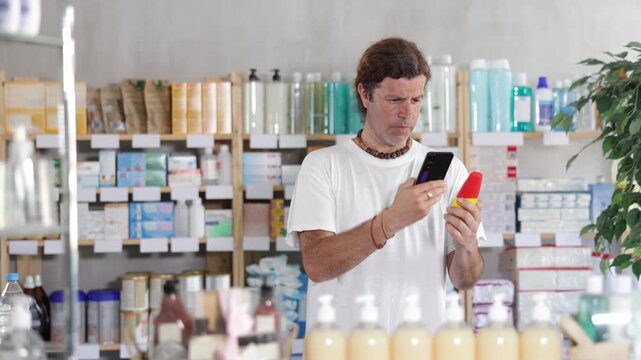 Man stands in a pharmacy and scans the barcode of a mosquito repellent on his phone. Buyer pays for purchases using a QR code in a European pharmacy. High quality 4k footage