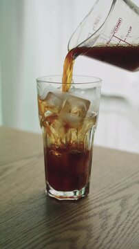 Closeup of Pouring Black Coffee into Glass with Ice Cubes, Making Iced Americano in Morning Routine.