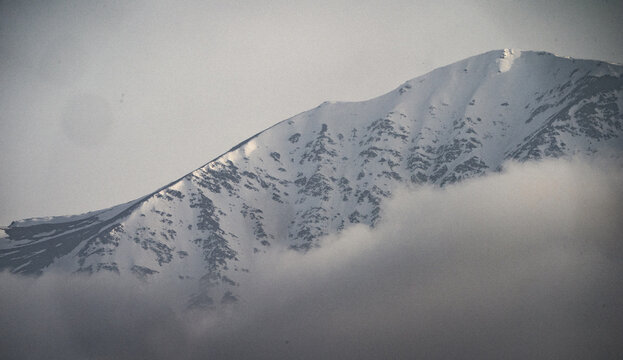 View of the snow-capped mountain peak of Zaamin National Park with rugged slopes partially obscured by low-hanging clouds in Zaamin, Jizzakh Region, Uzbekistan.