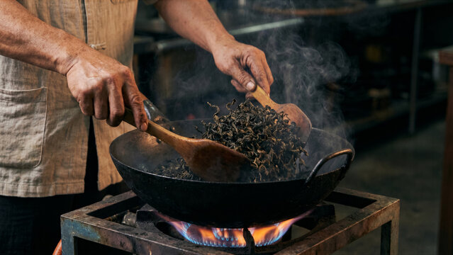 Close up of Taiwanese tea master hand firing oolong tea leaves in heated iron wok smoke photo