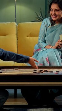 Indian kid playing carrom with grandparents in modern home indoors, elderly grandmother and grandfather enjoying board game with child, family bonding, traditional Indian lifestyle, fun, joy