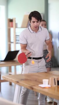 Several office staff are playing ping pong game to pass working break time. In spacious, bright office located on high floor of business center, people play ping pong during break.