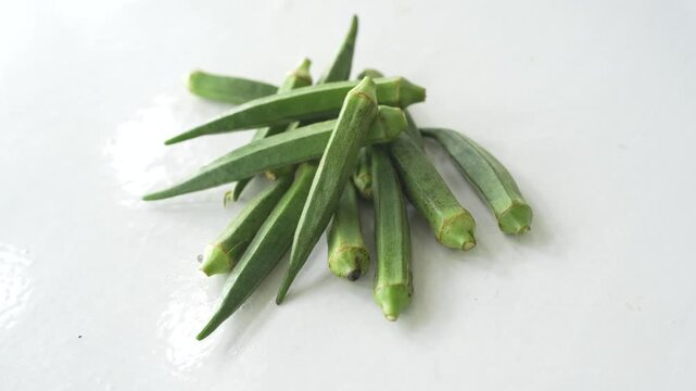 Fresh green okra pods placed on a clean white surface, showcasing natural freshness and healthy vegetable ingredients. Ideal for concepts of home cooking, nutrition, organic produce, and agriculture