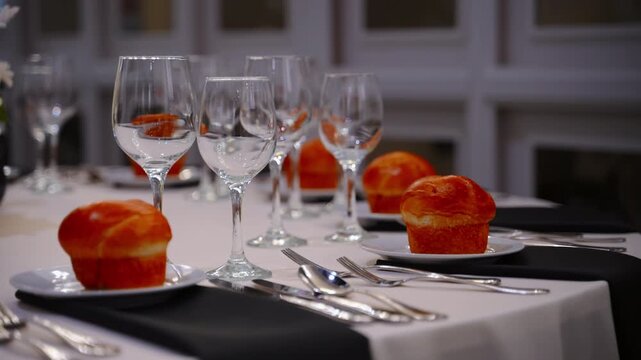 Elegant table setting prepared for guests at a traditional Jewish wedding reception. Fine dining arrangement with wine glasses and fresh bread rolls 