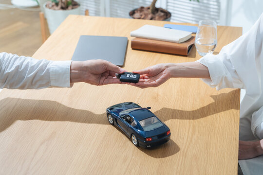 車のキーを受け取る女性。レンタカー、納車、ディーラー、スマートキー、ワイヤレスキー、ドライバー