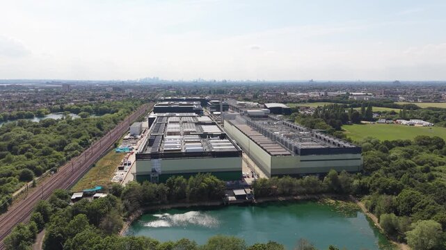 Aerial view of a large data center facility surrounded by green trees and a small pond in the suburbs of London, London, United Kingdom.