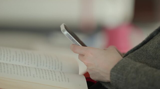 A close-up of a person's hand holding a stylus or pen over a tablet or notebook in a bright indoor setting suggesting note-taking or digital drawing.