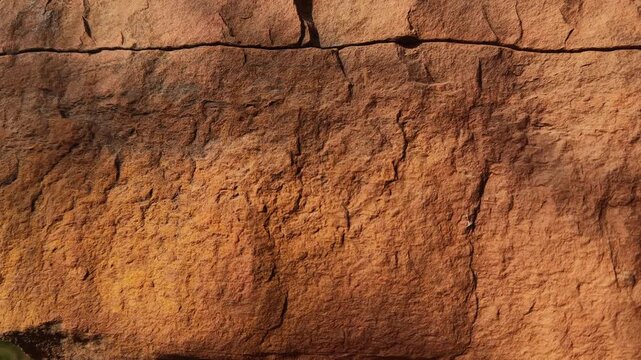 Slow jib down movement revealing weathered sandstone surfaces marked by natural cracks erosion patterns and rugged geological textures on an exposed rock face