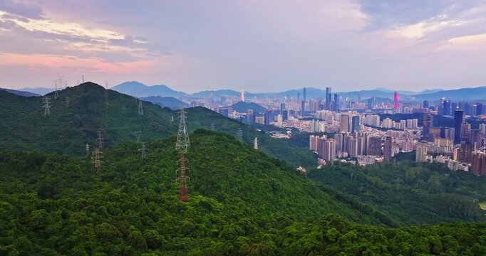 Aerial view of high-voltage power transmission lines on green mountains with urban skyline in Shenzhen, China