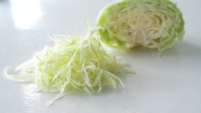 Fresh shredded cabbage with a halved cabbage placed on a clean white surface, highlighting healthy vegetable ingredients for salads, cooking, and meal preparation. Ideal for nutrition and fresh food 